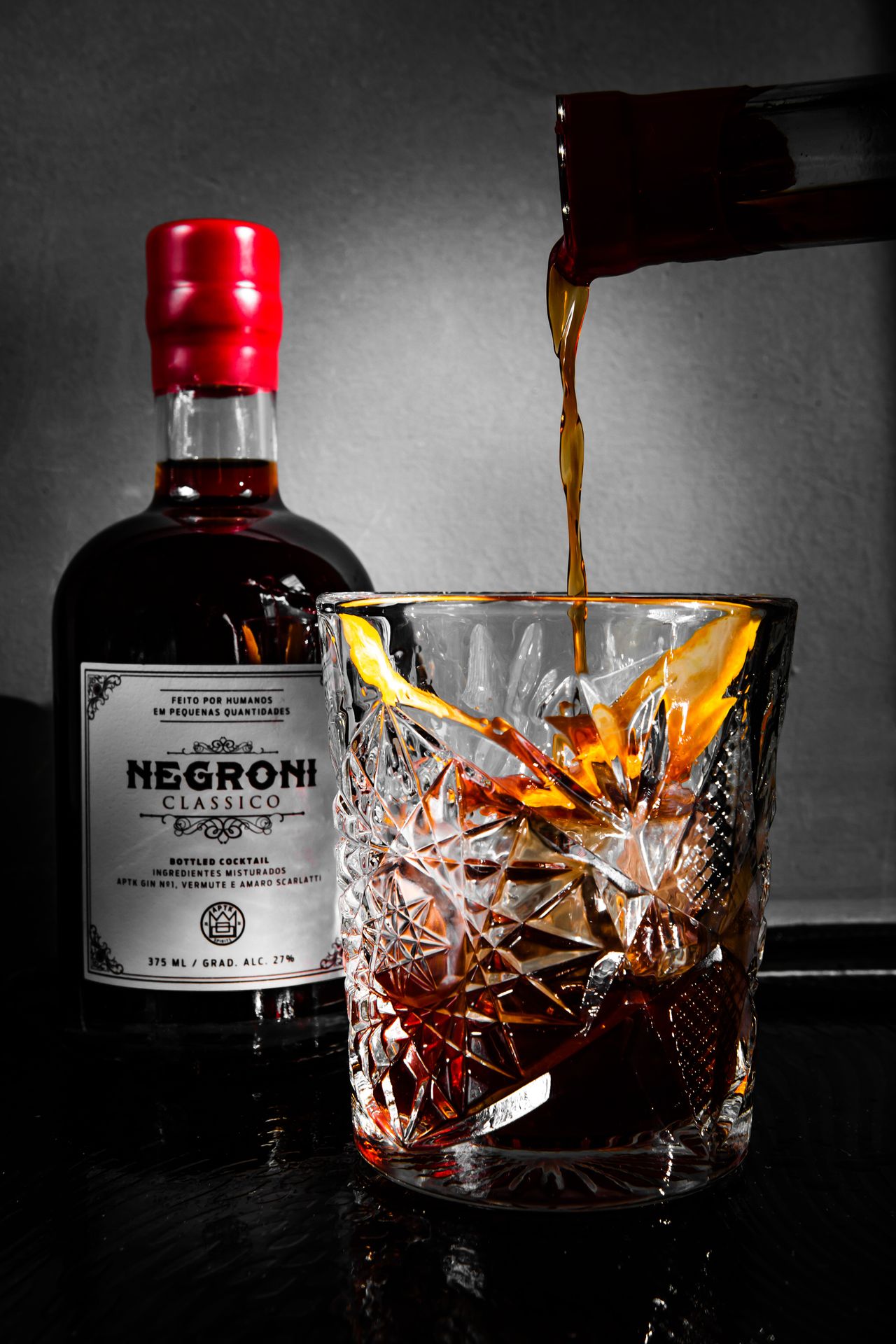 Negroni sendo servido em copo de cristal ao lado da garrafa